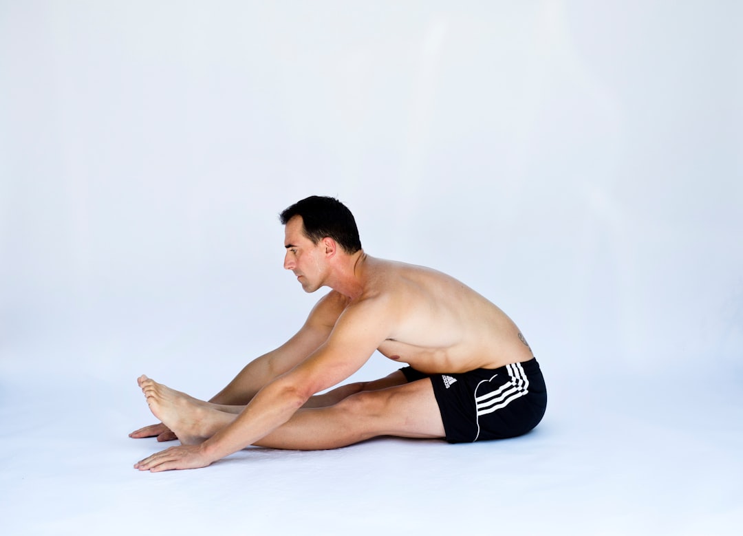 Person performing back stretch on exercise mat while focusing on proper posture, supervised by physical therapist